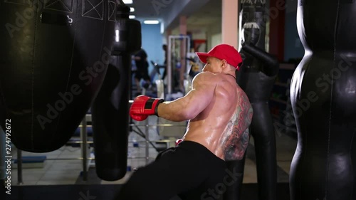 Handsome young man with a bare torso in a red cap and boxing gloves boxing on goal. Wide angle, Prores, Slow Motion photo