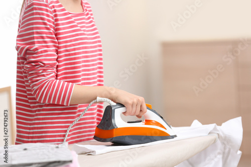 Young woman ironing clean laundry on board indoors, closeup. Space for text