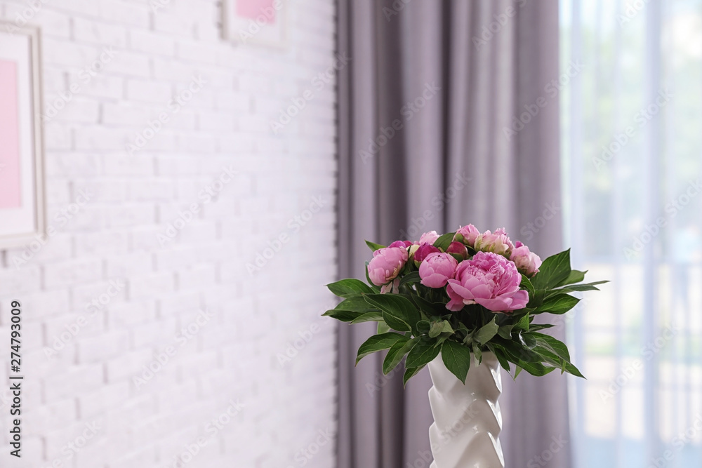 Fototapeta premium Vase with bouquet of beautiful peonies at white wall in room, space for text