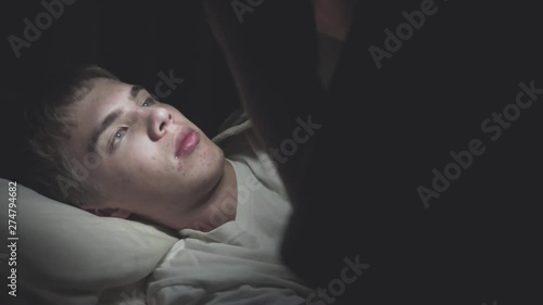 Male teenager lying on his bed while scrolling through social media on his phone. The camera pans in from the darkness.