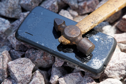 Broken glass of smartphone with hammer on gravel stones. Selective focus