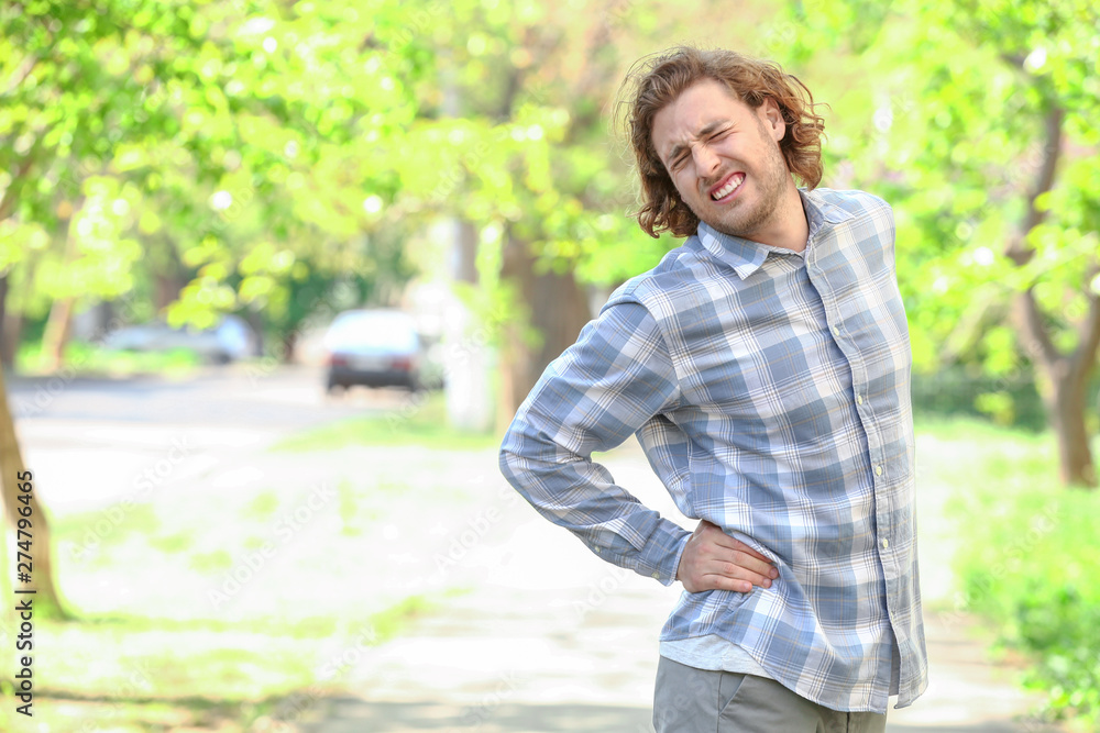 Young man suffering from back pain outdoors Young man suffering from back pain outdoors