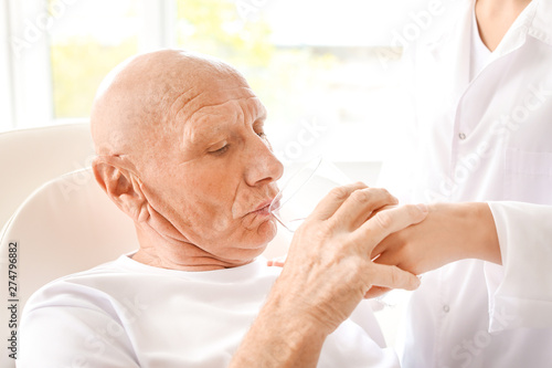 Doctor giving water to elde...