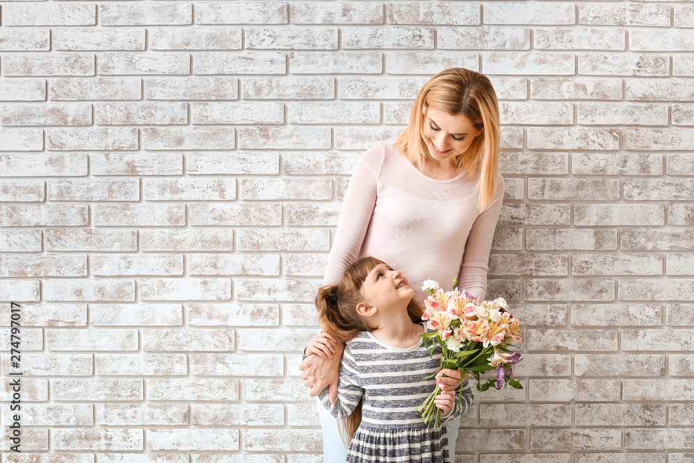 Little girl greeting her mother with bouquet of flowers against brick wall