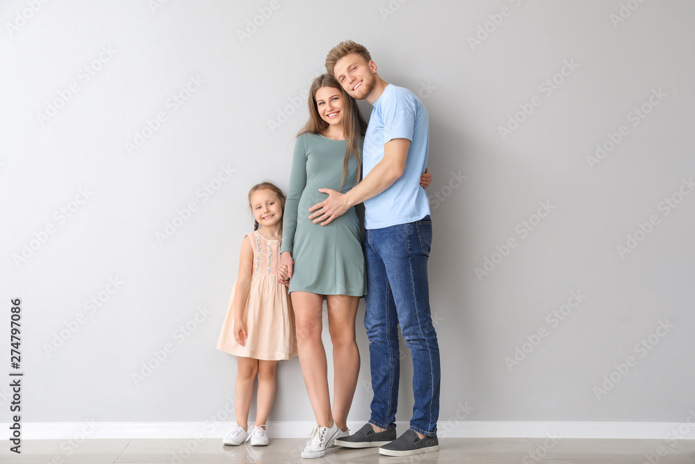 Beautiful pregnant woman with her family near light wall Beautiful pregnant woman with her family near light wall