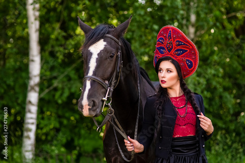Gorgeous Caucasian Model in Russian Kokoshnik Holding Thoroughbred Horse Against Nature Background.