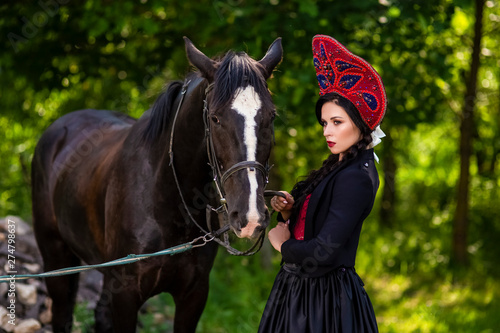 Fashion Model in Russian Kokoshnik Holding Thoroughbred Horse Against Nature Background.