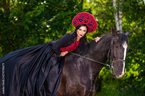 Gorgeous Fashion Model in Russian Style Kokoshnik Straddling On the Thoroughbred Horse. Posing Against Nature Background.