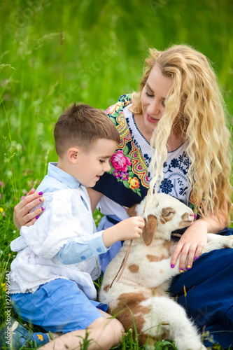 Smiling Mother with Her Little Happy Son and Cub of Newborn Lamb Posing Outdoors on Nature Background.