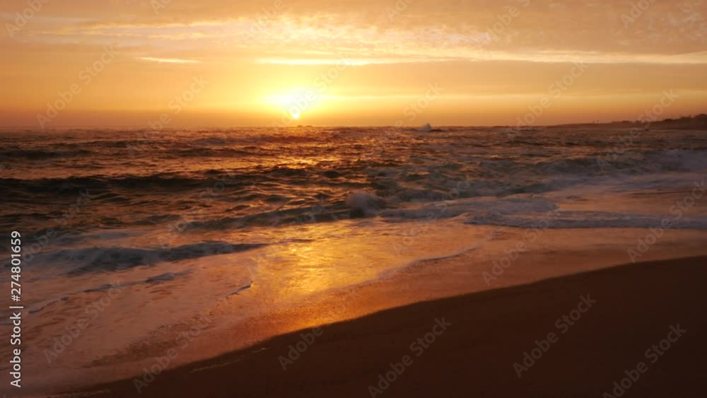 Low angle shot over beach at sunset with vivid orange sky and reflections on water Low angle shot over beach at sunset with vivid orange sky and reflections on water