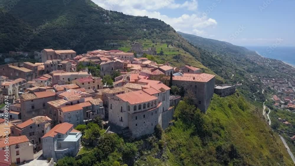 Aerial view of ancient city on hill top overlooking sea coast village and mountains. Drone camera flies over old masonry buildings with tiled roofs, sunny day in Calabria, Italy Aerial view of ancient city on hill top overlooking sea coast village and mountains. Drone camera flies over old masonry buildings with tiled roofs, sunny day in Calabria, Italy