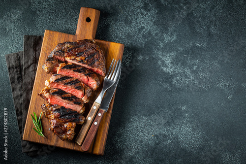 Sliced steak ribeye, grilled with pepper, garlic, salt and thyme served on a wooden cutting Board on a dark stone background. Top view with copy space. Flat lay