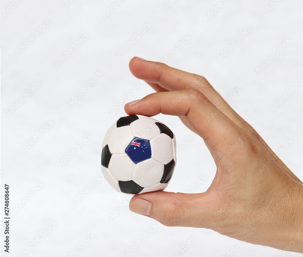 Mini ball of football in hand and one black point of football is Australia flag, hold it with two finger on white background.