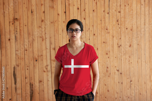 Woman wearing Denmark flag color shirt and standing with two hands in pant pockets on the wooden wall background. photo