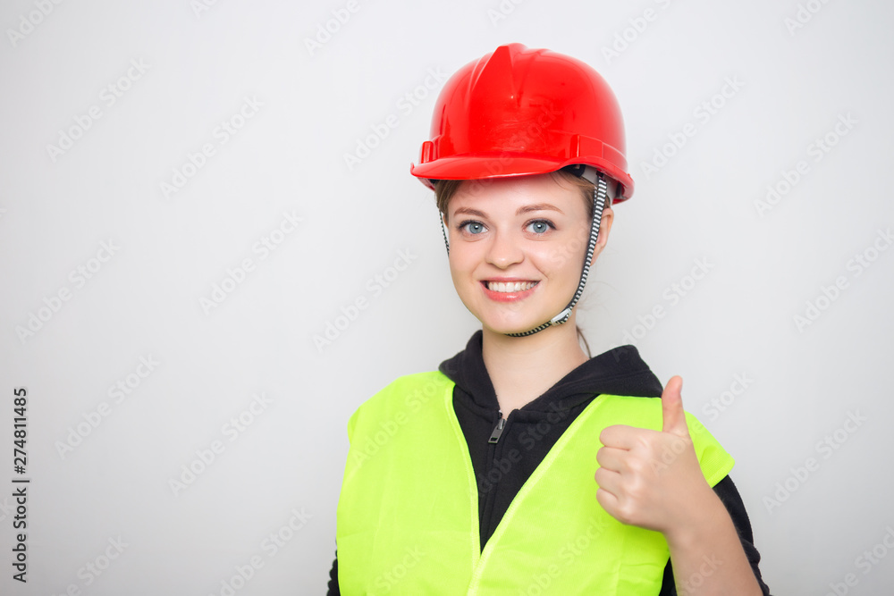 Young caucasian woman wearing red safety hard hat and reflective vest, smiling with thumbs up