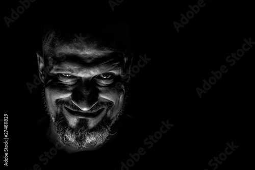  Face with a bearded man grimace against a dark background with sharp shadows. Comedic, fabulous villain or negative character conception with copy space. photo