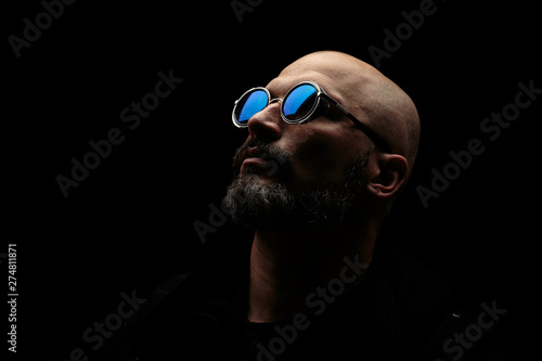 Bald man with grey beard in sunglass on dark background