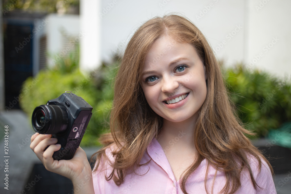 Portrait of young caucasian woman photgrapher holding a digital camera, smiling