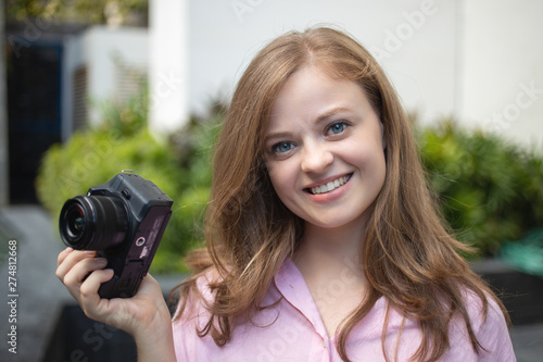 Portrait of young caucasian woman photgrapher holding a digital camera, smiling photo