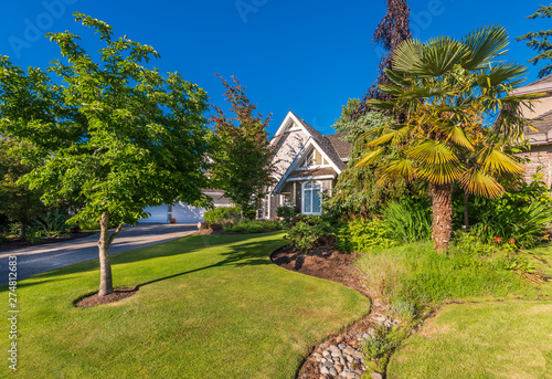 Beautiful exterior of newly built luxury home. Yard with green grass and walkway lead to front entrance. © karamysh