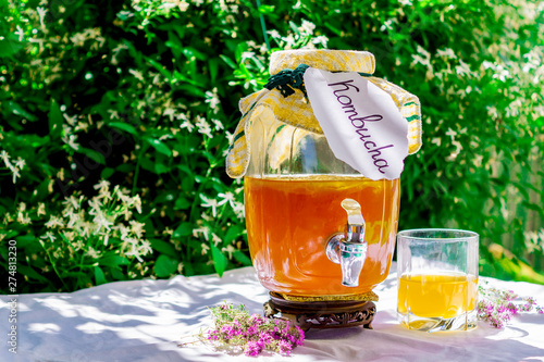 Refreshing kombucha tea with thyme in a glass old vintage bottle and a glass, with label written kombucha on it on backdrop of blurred flowers. Healthy natural probiotic flavored drink. Copy space photo