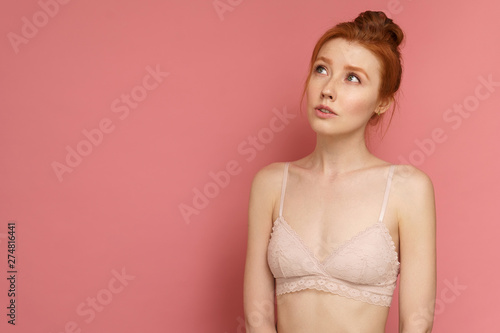 Young redhead woman wearing lace bra with a bun on her head looks up thinking of something