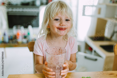 Little girl frinking a glass of healthy smoothie in the kitchen photo