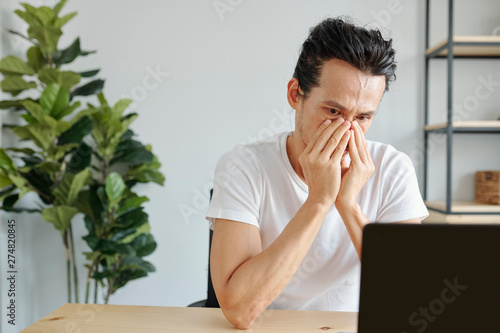 Portrait of almost crying Asian man reading e-mail with bad news on laptop screen