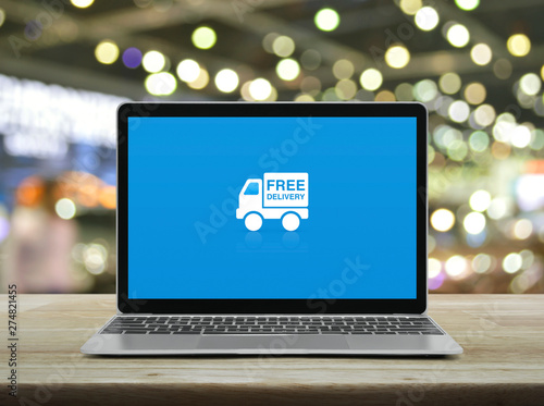 Free delivery truck flat icon with modern laptop computer on wooden table over blur light and shadow of shopping mall, Business transportation online concept