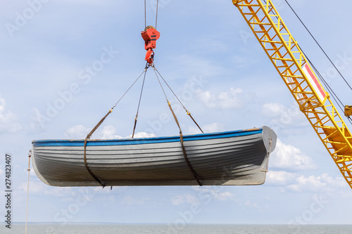 Rowing wooden boat is launching into the sea by using crane