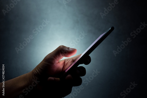 silhouette hand holding and touching a mobile phone screen in the dark darkness against dark blue background