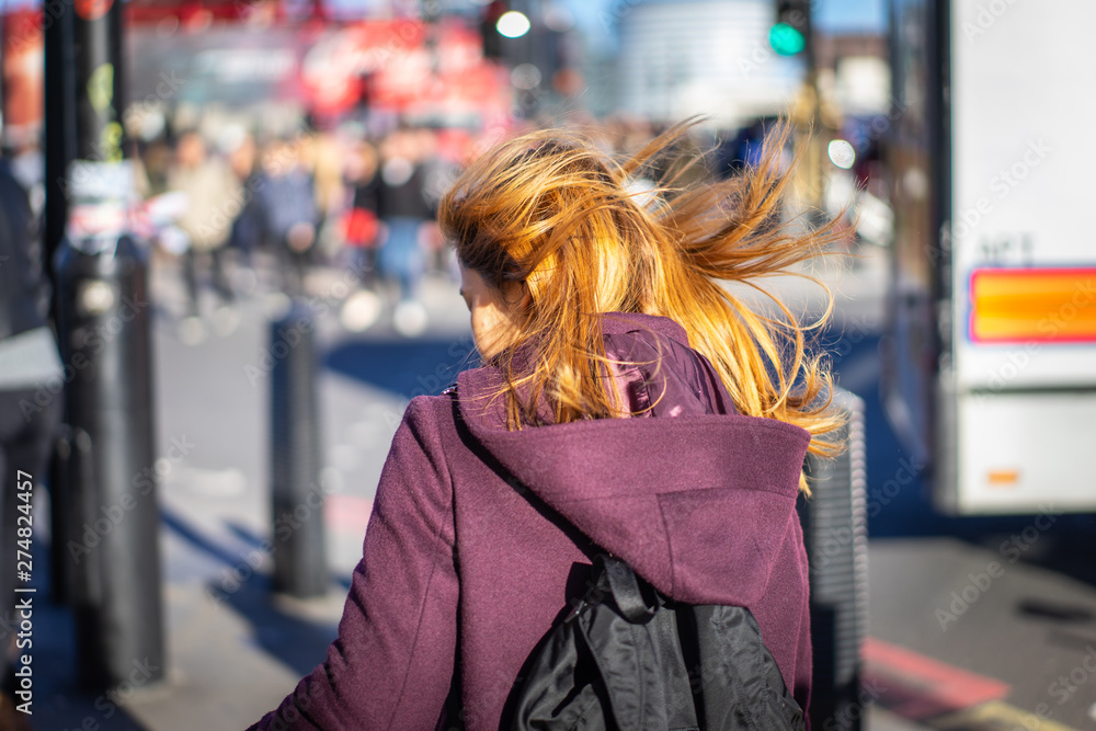 Back view of ginger girl with windy hair in purple coat walking on city street at Westminster Bridge, England Back view of ginger girl with windy hair in purple coat walking on city street at Westminster Bridge, England