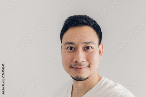 Smile man is taking selfie of himself with white t-shirt and grey background.
