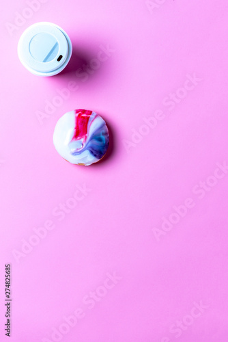 Top-down-view of a coffee and a doughnut on a bright pink background