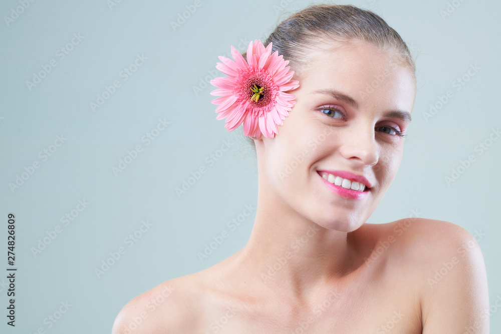 Portrait of attractive young woman with beautiful glowy skin posing with pink flower in her hair Portrait of attractive young woman with beautiful glowy skin posing with pink flower in her hair
