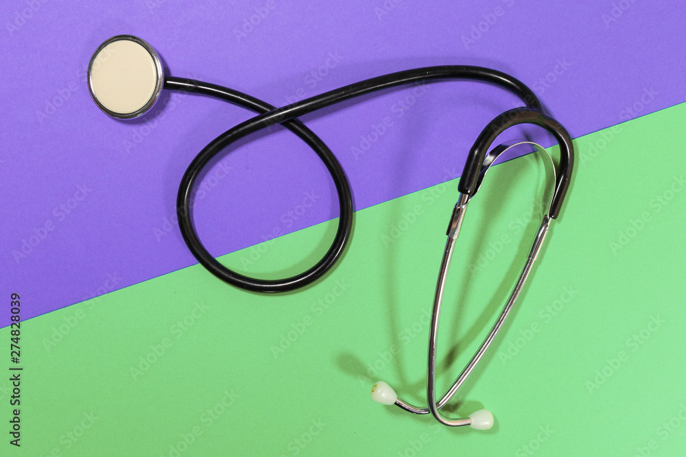 A stethoscope is laying on a purple and green surface A stethoscope is laying on a purple and green surface