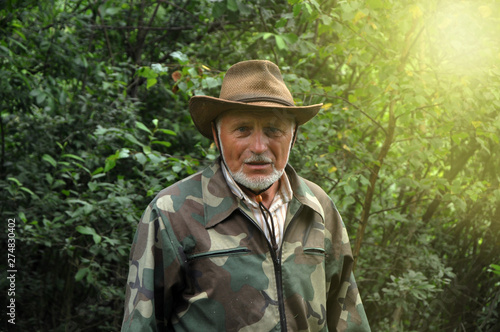 Middle aged traveler. Portrait of a handsome adult man with a gray beard and hat in camouflage clothing.