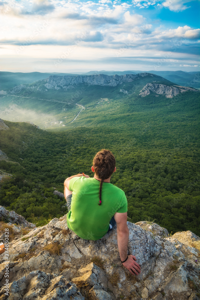 Naklejka premium Young man hiker sitting on a cliff edge