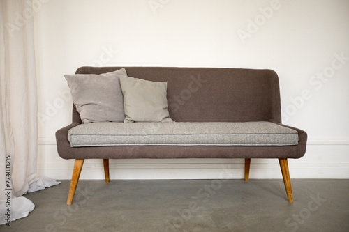 Comfortable stylish sofa with grey pillows and insert on wooden legs in light room