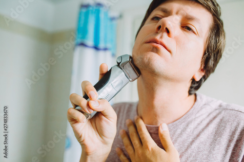 Photography Young man shaving his face using an electric razor  in the bathroom