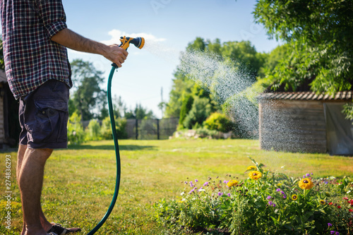 Photo Hipster young man watering plants in a country house, summer and garden care