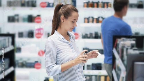 Beautiful girl chooses perfume in cosmetics shop, sniffs it, slow motion