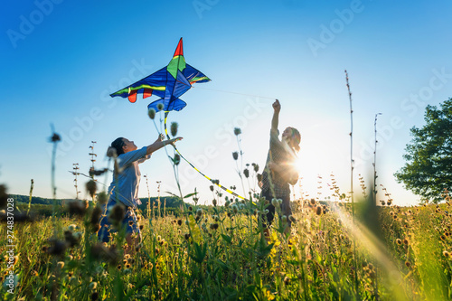 Fotografie young happy beautiful couple flying a kite in a summer field, summer happiness a