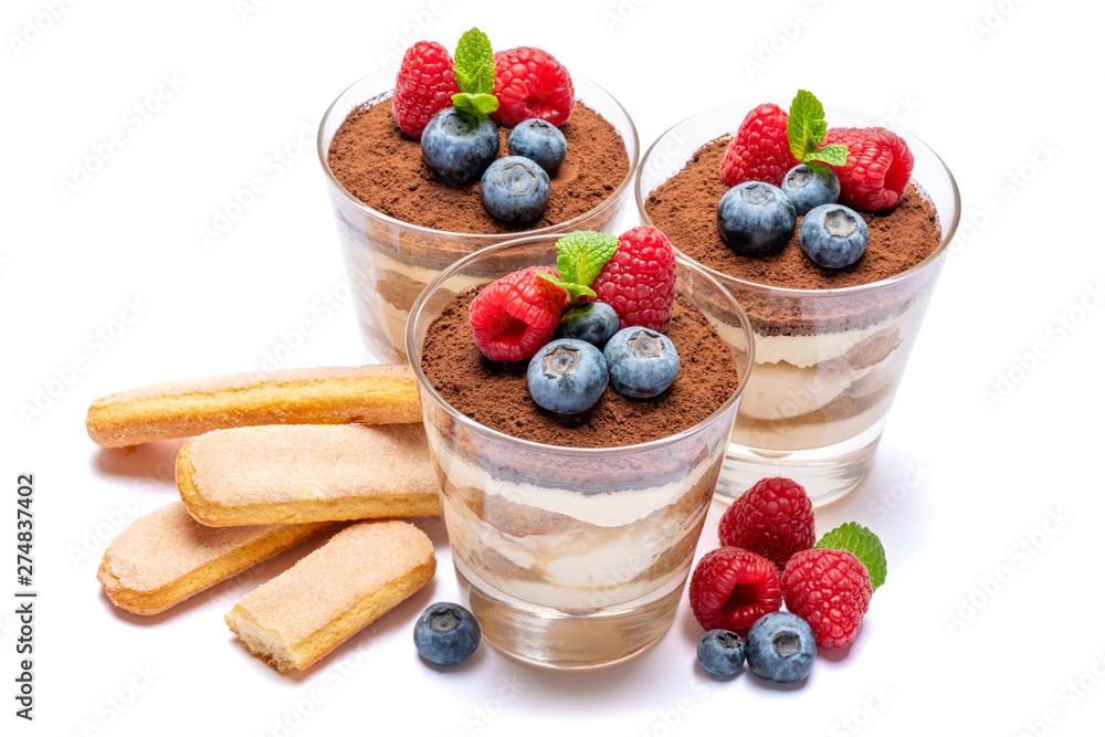 Classic tiramisu dessert with blueberries and raspberries in a glass and savoiardi cookies isolated on a white background with clipping path Classic tiramisu dessert with blueberries and raspberries in a glass and savoiardi cookies isolated on a white background with clipping path