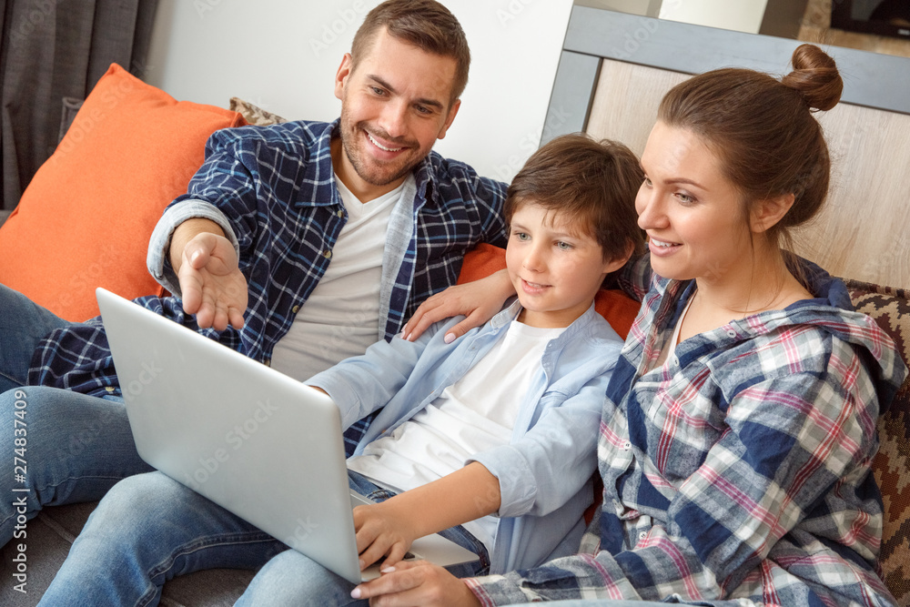 Family at home sitting on sofa in living room together searching info in internet on laptop pointing at screen joyful Family at home sitting on sofa in living room together searching info in internet on laptop pointing at screen joyful