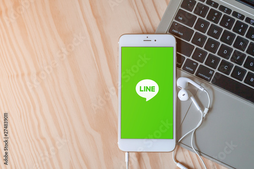 Rayong, Thailand, May 19, 2019: Line logo on smartphone screen placed on laptop keyboard on wood background with earphones and copy space