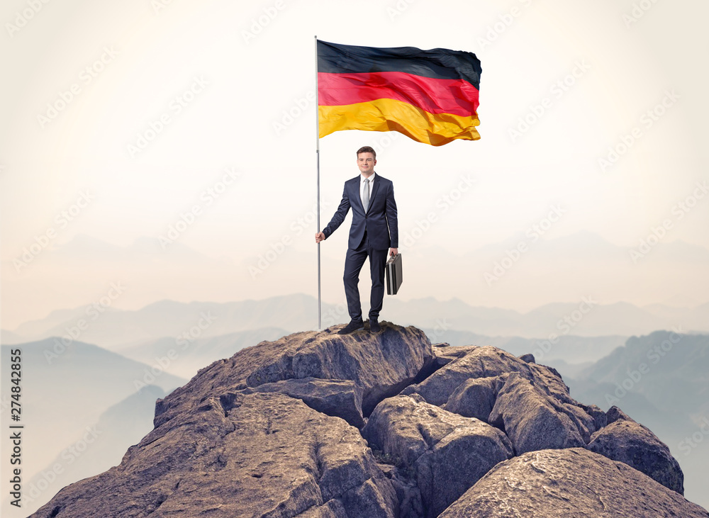 Obraz premium Successful businessman on the top of a mountain holding victory flag 