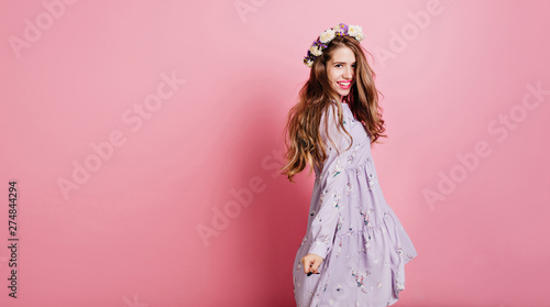 Excited dark-haired girl looking to camera with smile. Indoor portrait of adorable woman in flower wreath and purple dress.