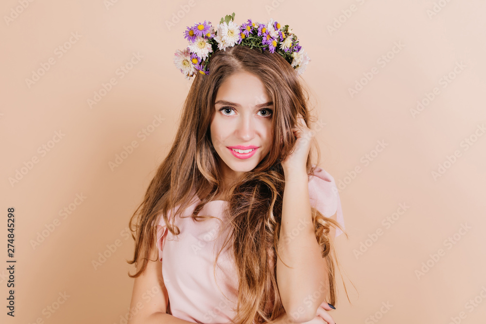 Close-up portrait of magnificent girl with long dark hair posing on light background. Pretty female model wears cute flower wreath laughing to camera during photoshoot. Close-up portrait of magnificent girl with long dark hair posing on light background. Pretty female model wears cute flower wreath laughing to camera during photoshoot.