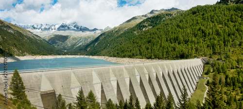 Big concrete dam with scenery of lake, forest and high mountains.